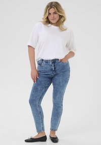 Camiseta blanca de manga corta combinada con unos jeans de mezclilla azul de tiro alto, con un ligero desgaste, y unas bailarinas negras.