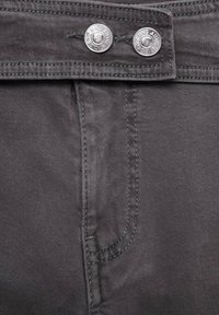 Primo piano della cintura di jeans grigi in denim con due bottoni metallici argentati etichettati "AUTHENTIC DENIM MNG."