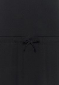 Svart plagg i mjukt, lättviktigt material. Har en dragsko i midjan som skapar en åtsittande design. Slät yta utan mönster.