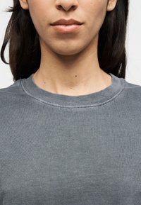 Sudadera gris de algodón con cuello redondo y textura acanalada, presenta costuras visibles y un corte holgado.