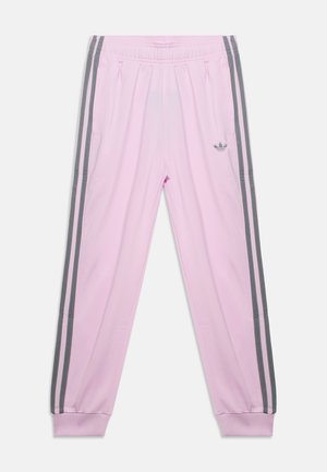 Pantalon de survêtement rose clair avec taille élastique, bandes latérales gris foncé, poches avant et logo Adidas sur la cuisse gauche.