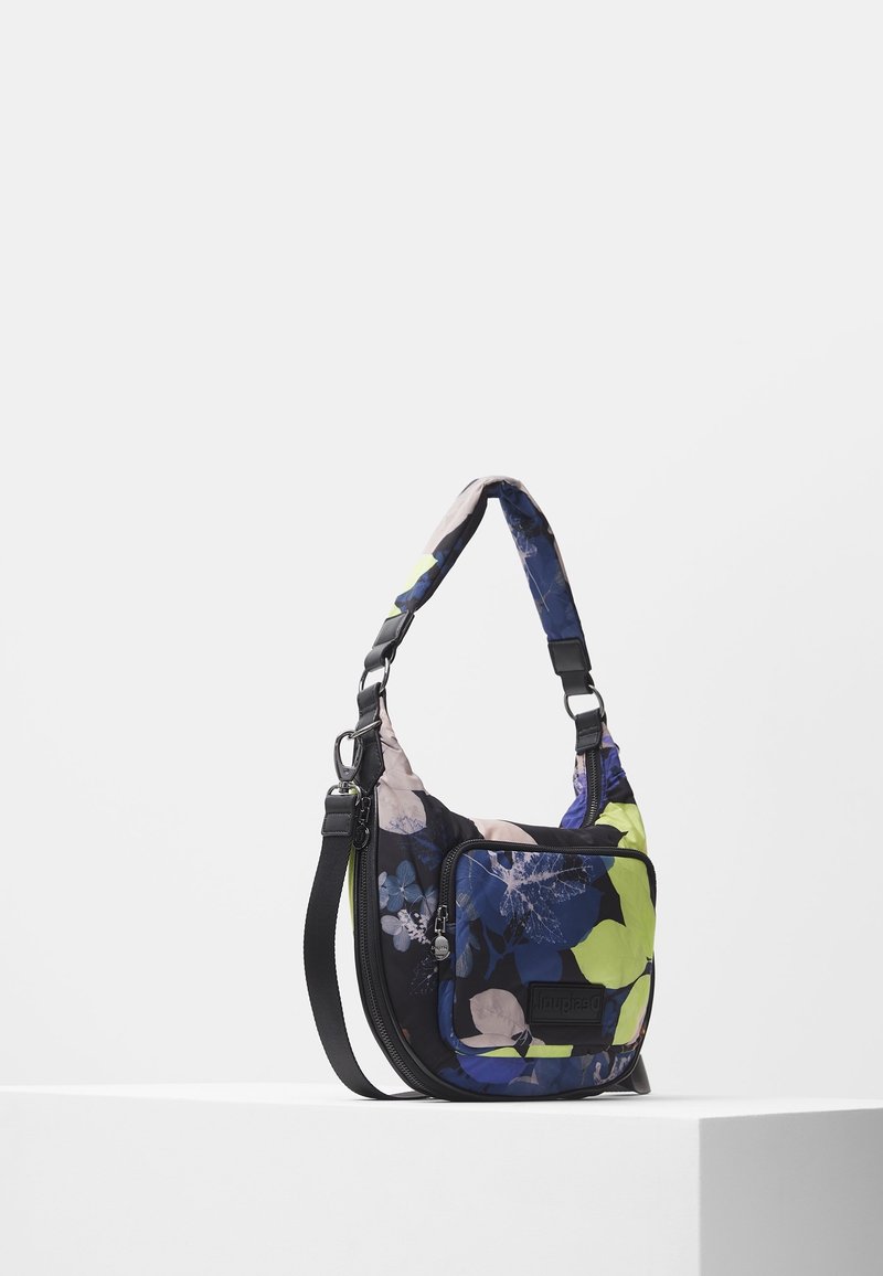 Torebka na ramię z regulowanym czarnym paskiem, wzór kwiatowy w kolorach niebieskim, zielonym i beżowym, przednia kieszeń zapinana na suwak oraz wyściełana rączka na białym tle.