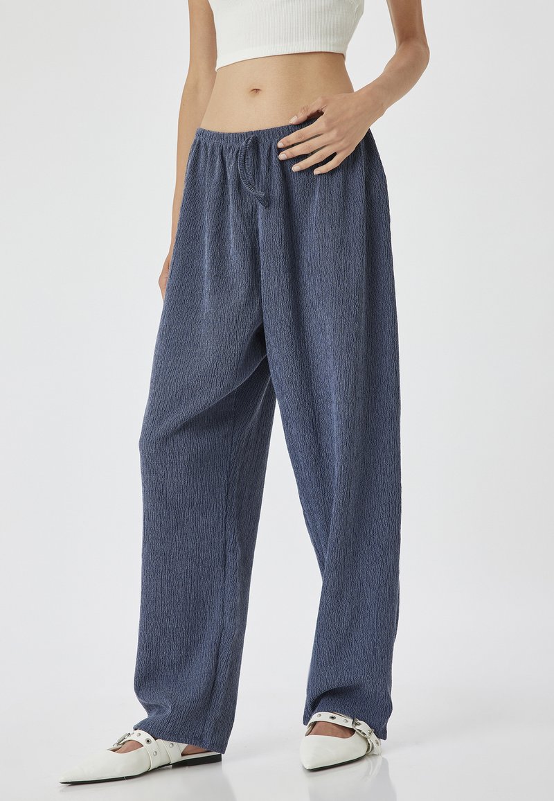 Pantalons navy texturés, amples, avec une taille élastique et un détail de cordon de serrage. Associés à des chaussures blanches à talons pointus.