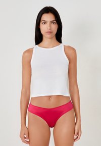Weißes, kurzes Tanktop mit Rundhalsausschnitt, kombiniert mit roter Satin-Bikiniunterwäsche mit feinem, gewelltem Rand.
