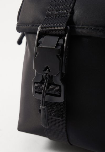 Borsa nera in nylon con una prominente fibbia nera in plastica e tracolla regolabile, con cuciture testurizzate e un cordino per una chiusura sicura.