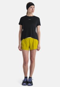 Camiseta deportiva negra, pantalones cortos amarillos con cintura elástica, zapatillas negras con detalles púrpuras y una diadema negra. Diseño simple y funcional.