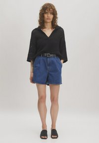 Zwarte gebreide v-hals top met losse mouwen, gecombineerd met blauwe denim shorts en zwarte slidesandalen. Details omvatten een taille met riem.