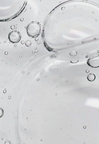 Líquido claro con burbujas esféricas de diversos tamaños, flotando en un entorno translúcido. Textura suave y reflexiones sutiles presentes.