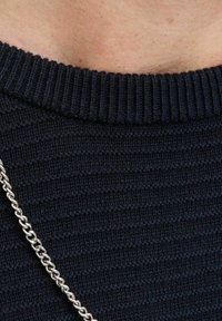 Pull en tricot bleu marine avec un col rond côtelé et un motif texturé subtil. Une chaîne en argent est visible sur le tissu.