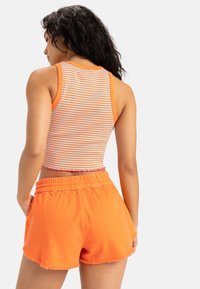 Striped crop top with orange and white lines; paired with orange shorts featuring a frayed hem and elastic waistband.