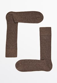 Braune gerippte Socken aus weichem Material, mit einer glatten Textur, abgerundeten Zehen und kontrastierenden Akzenten an Bündchen und Spitze.