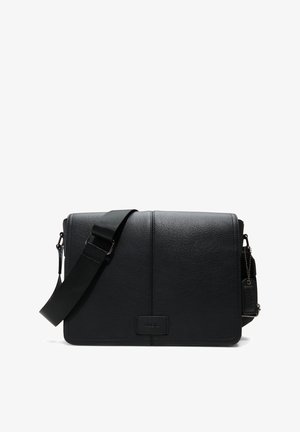 Bolso mensajero negro de cuero con superficie texturizada, correa ajustable y una pequeña etiqueta. Presenta una forma rectangular simple.