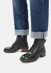 Černé kožené kotníkové boty s šněrováním, kulatou špičkou a dřevěným podpatkem. Ozdobené bočním zipem a detailním kulatým přezkou.