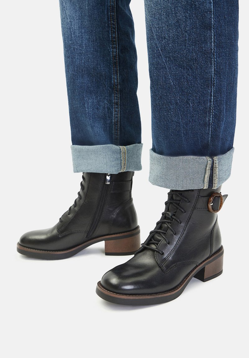 Černé kožené kotníkové boty s šněrováním, kulatou špičkou a dřevěným podpatkem. Ozdobené bočním zipem a detailním kulatým přezkou.