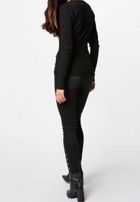 Top negro de manga larga con un diseño ajustado, combinado con unos jeans negros ajustados que tienen detalles de botones en los tobillos. Textura suave en toda la prenda.