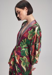 Lange, fließende Robe mit einem lebhaften Blumenmuster und tiefem V-Ausschnitt. Aus Seide gefertigt, mit weiten Ärmeln und geometrischem Saum.