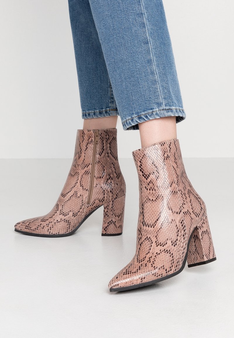 Bottes à la cheville, bout pointu, talons blocs imprimé serpent rose, portées avec un jean bleu raccourci.