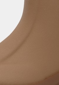 Tige de botte en cuir lisse couleur tan avec une texture à grain fin et une couture arrondie près de la semelle.