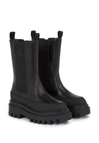 Botas negras de tobillo con suela gruesa, hechas de cuero y tela con paneles laterales elásticos. Presentan un logotipo en el eje exterior y una suela texturizada.