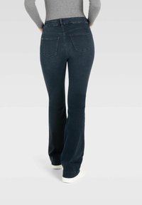 Dunkelblaue, ausgestellte Jeans mit mittelhohem Bund, zwei Gesäßtaschen und minimalen Nähakzenten. Tragen mit weißen Sneakers.