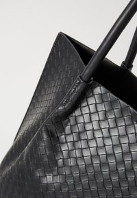 Borsa a spalla in pelle intrecciata nera con superficie testurizzata, dotata di due robusti manici e design a apertura superiore.