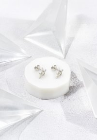 Silverpar av origami-cranestudörhängen på en cirkulär vit display, omgiven av klara trianglar. Slät textur, intrikat design.