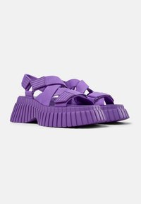 Sandali platform viola con ampie fasce elastiche e suola in gomma rigata. Presentano un design chunky e testurizzato per stabilità e supporto.