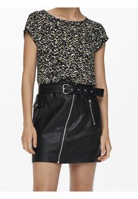 Blusa de manga corta con un patrón de ondas en negro y beige, combinada con una mini falda de cuero negra con cremallera frontal y cinturón.