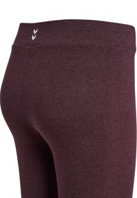 Bordeaux leggings met een brede tailleband, gemaakt van rekbare stof. Voorzien van subtiele witte chevronaccenten nabij de tailleband.