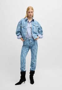 Ljusblå denimjacka med två bröstfickor, tillsammans med matchande mönstrade jeans. Långärmad randig skjorta under. Svarta ankelboots.