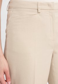 Beige broek met een gestructureerde stof met een ruitpatroon, een slim fit en zijzakken. De tailleband heeft riemlussen voor extra verbetering.