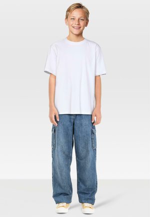 T-shirt bianco a maniche corte abbinato a pantaloni cargo in denim blu chiaro, larghi, con tasche laterali e sneakers gialle.