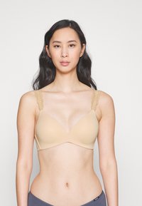 Beige bra with a smooth, molded cup design. Features lace-accented straps and a V-shaped neckline. Soft texture and seamless construction.