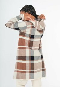 Manteau à carreaux présentant des nuances de brun, crème et gris, avec une capuche, des manches longues et des poches latérales. Fabriqué en tissu texturé.