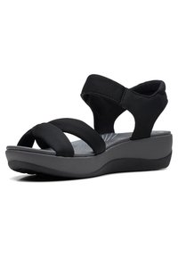 Schwarze Sandalen mit gepolstertem Fußbett, ausgestattet mit zwei breiten Stoffriemen und einer dicken, strukturierten Keilsohle für Unterstützung und Komfort.