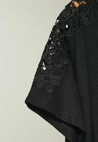 Indumento nero con maniche corte decorate da intricate rifiniture in pizzo floreale nero lungo le spalle. Texture liscia, design moderno.