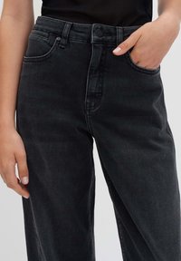 Jeans in denim nero a vita alta con una vestibilità rilassata, caratterizzati da cinque tasche, chiusura con bottone e leggere sfumature sul tessuto.