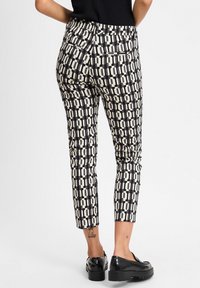 Pantalones estampados con un diseño ajustado en negro y crema, que presentan un estampado geométrico, piernas estrechas, bolsillos y corte a la altura del tobillo.