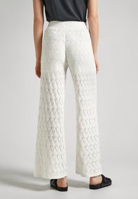 Pantalones de pierna ancha blancos con un patrón de punto que presenta formas de diamante. La tela es texturizada, con una cintura alta y una ligera calidad translúcida.