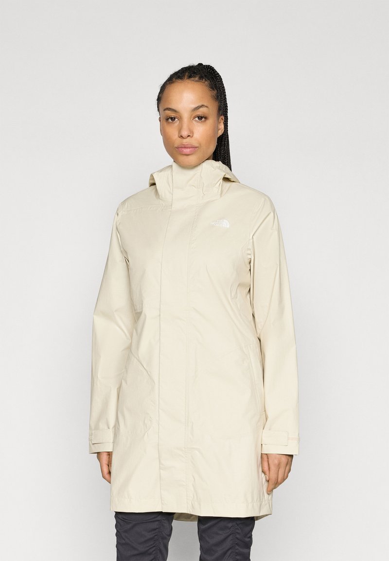 Veste de pluie beige avec un col montant, une fermeture éclair et des poches latérales. Fabriquée en matériau lisse et léger, avec un marquage minimal.