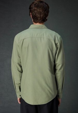 Camicia a maniche lunghe verde oliva con orlo curvo, polsini abbottonati e colletto semplice; texture liscia con una finitura leggermente opaca.
