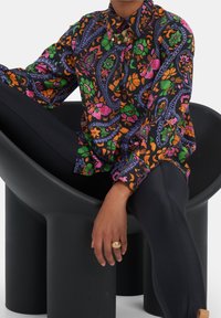 Langarm, met kraag, shirt in zwart met levendige bloemen- en paisleypatronen in roze, groen en oranje. Gestyled met zwarte legging.