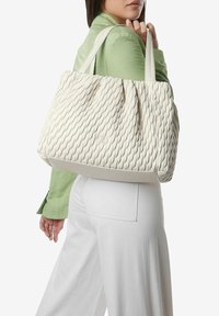 Crème kleurige tote bag met een golvend patroon, voorzien van twee stevige handvatten en een gestructureerde basis. Het materiaal lijkt zacht en buigzaam.
