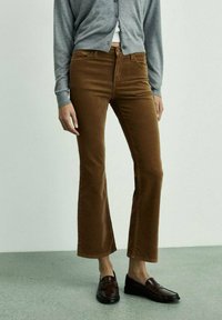 Brown flared corduroy pants with a smooth texture, featuring pockets and a mid-rise fit, paired with dark loafers and a gray cardigan.