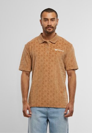 Braunes Polohemd mit Textur und Kragen, versehen mit einem Rautenmuster und Logo, kombiniert mit hellblauen Jeansshorts.