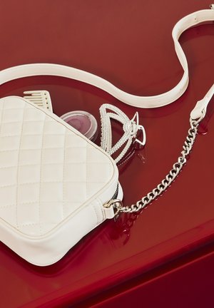 Borsa bianca trapuntata con tracolla a catena, dotata di chiusura con zip. Accompagnata da un accessorio per capelli con dettagli in argento e un pettine.