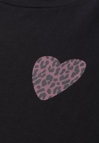 Forme de cœur avec imprimé léopard rose et gris sur un fond en tissu noir, ressemblant à un motif sur des vêtements.