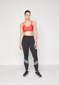 Röd sportbh med svart logoband, kombinerad med svarta leggings med grå accent, bärs med svarta löparskor. Enkel, åtsittande design.