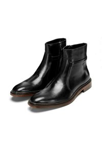 Botas de tobillo de cuero negro con un diseño elegante, que cuentan con cremalleras laterales y una suela de goma marrón. Textura suave con detalles de costura mínimos.