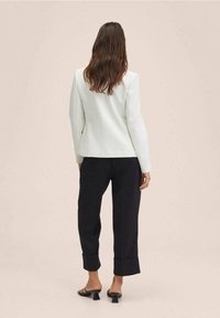 White fitted blazer with long sleeves, tailored design, paired with black wide-leg trousers, featuring rolled cuffs and open-toe black heels.